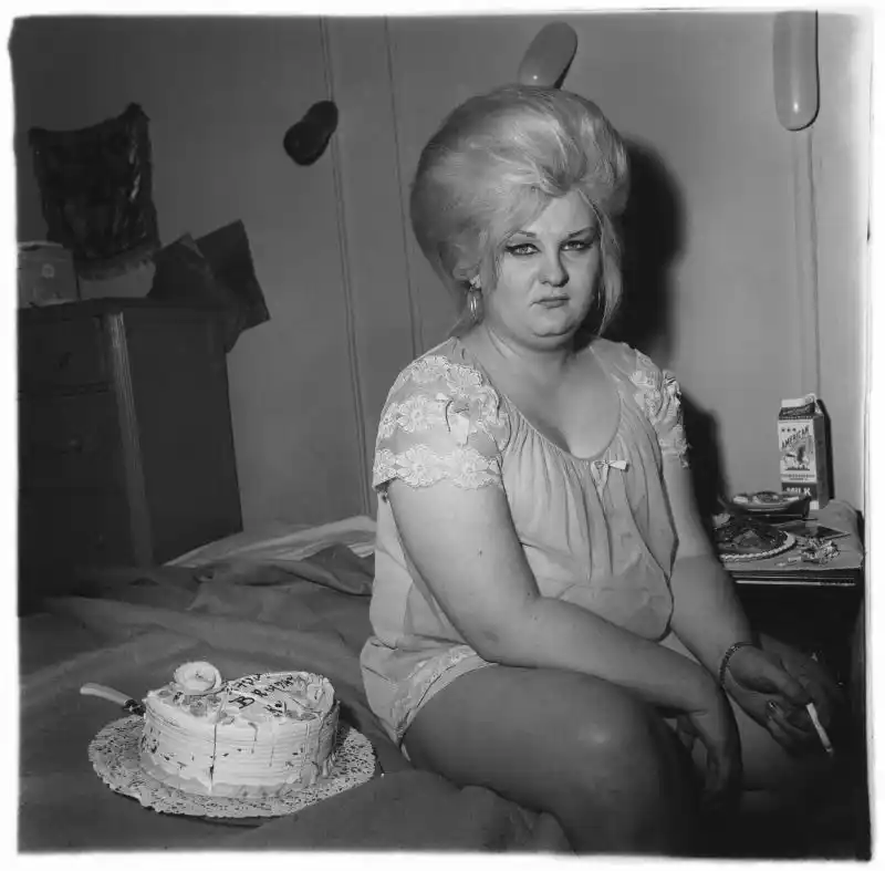 Retrato en blanco y negro de una persona sentada en una cama junto a una tarta